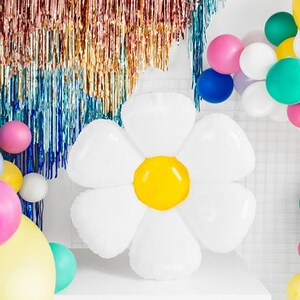 May include: A large white balloon shaped like a daisy with a yellow center. The balloon is surrounded by a variety of colorful balloons, including pink, green, blue, and yellow.