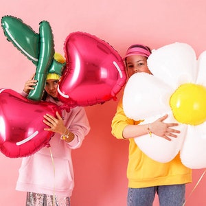 May include: Two children holding large foil balloons. One child is holding a red cherry balloon and the other is holding a white daisy balloon.