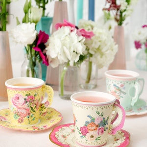 May include: A set of three floral teacups and saucers. The teacups are made of paper and have a floral design. The saucers are also made of paper and have a pink rim.