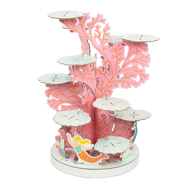 May include: A pink and white cardboard coral reef cupcake stand with a mermaid and seashells. The stand has five tiers for cupcakes.