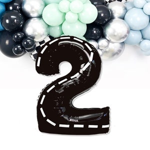 May include: Black number two balloon with a white checkered race track design. The balloon is surrounded by a garland of blue, silver, and black balloons.