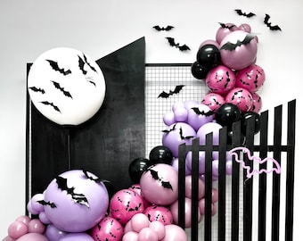 May include: A Halloween balloon display with a large white balloon adorned with black bat cutouts, and a cascade of purple, pink, and black balloons. The balloons are decorated with bat silhouettes. A black wooden structure and bat cutouts complete the festive display.