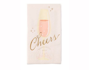 May include: Pink and gold paper napkins with a champagne glass and the text "Cheers Bachelorette Bash".
