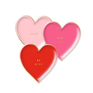 May include: Three heart-shaped plates with gold trim. The plates are pink, red, and a darker shade of pink. The plates have the following text: XOXO, KISS ME, and BE MINE.