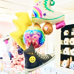 May include: A group of colorful foil balloons featuring a roller skate, a disco ball, a lightning bolt, a smiley face shoe, and a pink and white smiley face balloon.