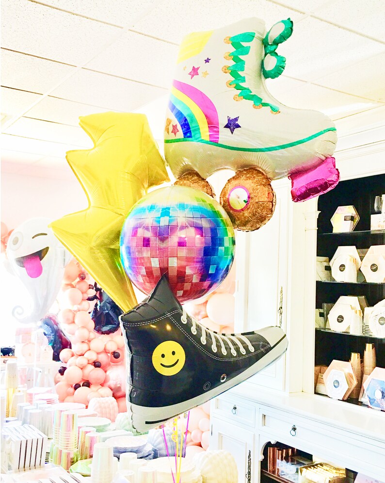 May include: A group of colorful foil balloons featuring a roller skate, a disco ball, a lightning bolt, a smiley face shoe, and a pink and white smiley face balloon.