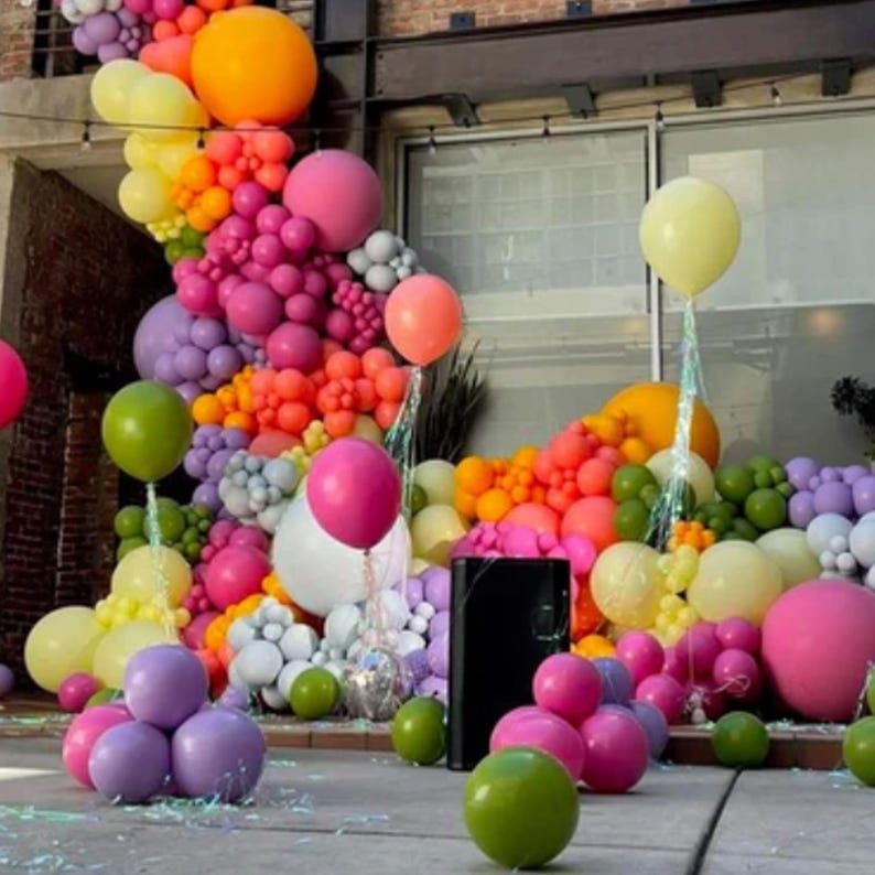 May include: A wall decorated with a rainbow of balloons in various sizes and colors, including pink, purple, green, yellow, orange, and red. The balloons are arranged in a cascading pattern, creating a festive and colorful backdrop.