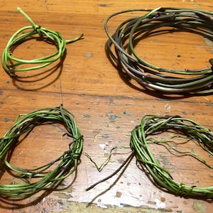 May include: Four different sizes of wreaths made from woven green vines. The wreaths are arranged on a wooden surface.