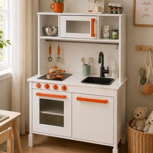 May include: A white wooden toy kitchen set featuring orange handles, a black sink, a stovetop with two pots, a microwave, and a coffee maker. The unit includes a hanging rail with utensils, a shelf with a milk carton, and a framed sign reading little chefs at play.