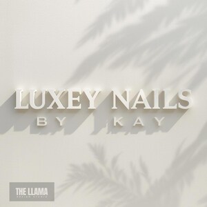 May include: A three-dimensional wall sign featuring the white text LUXEY NAILS BY KAY in a serif font. The letters cast distinct shadows on a light off-white wall, with soft palm leaf shadows overlaying the upper right portion of the display.