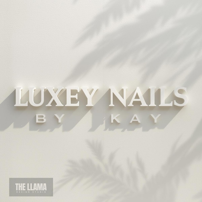 May include: A three-dimensional wall sign featuring the white text LUXEY NAILS BY KAY in a serif font. The letters cast distinct shadows on a light off-white wall, with soft palm leaf shadows overlaying the upper right portion of the display.