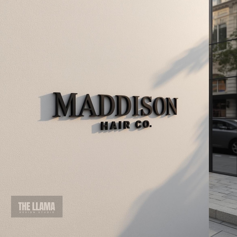 May include: A three-dimensional wall sign featuring the black text MADDISON HAIR CO. in a serif font. The letters are mounted on a smooth, light-colored wall, creating distinct shadows that emphasize the depth and relief of the signage.