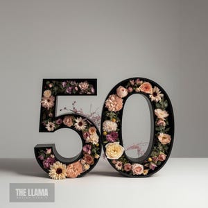 May include: Black wooden number 50, adorned with a variety of flowers in pink, peach, and cream hues. The flowers fill the inside of the numbers, creating a floral arrangement. The numbers are displayed on a white surface.