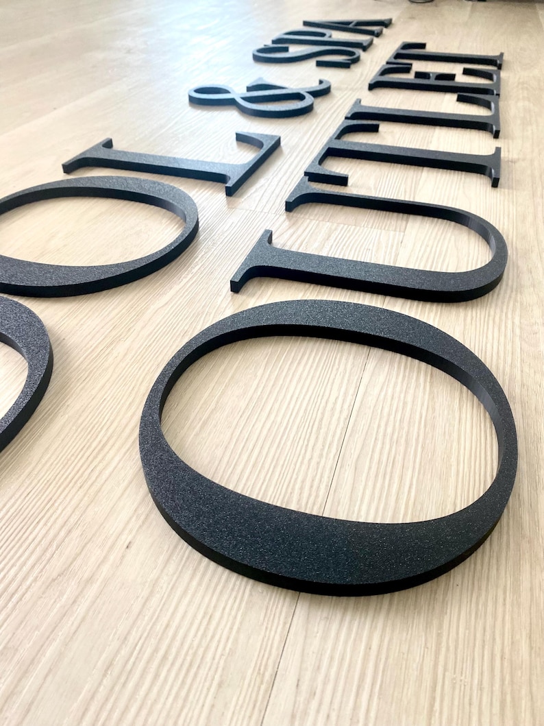 May include: A set of three-dimensional black letters with a textured finish spelling out the words POOL & SPA OUTLET. The letters are arranged in two rows, featuring a clean serif typeface with a distinct depth, creating a bold visual impact.