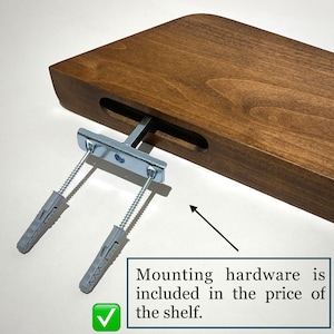 May include: A brown wooden floating shelf with a rectangular slot on the side. A silver metal mounting bracket is inserted into the slot, featuring two long threaded screws with grey plastic wall anchors attached. Text reads: Mounting hardware is included in the price of the shelf.
