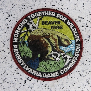 May include: Circular patch with a brown beaver illustration, green grass, and blue water. Text includes "PENNSYLVANIA GAME COMMISSION" and "WORKING TOGETHER FOR WILDLIFE". The year "1995" is also visible. The patch has a red border.
