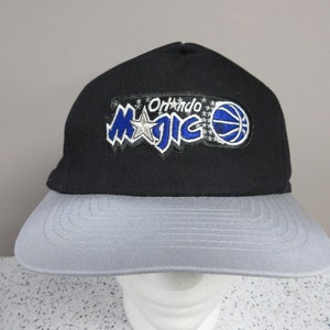 May include: Black and gray baseball cap featuring the Orlando Magic logo. The cap has a black crown and a gray brim. The logo includes the team name, a star, and a basketball.