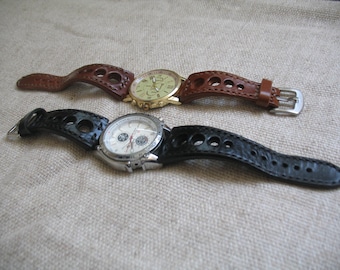 Puede incluir: Dos relojes de pulsera con correas de cuero. El reloj de arriba tiene una correa de cuero marrón con una esfera blanca y detalles dorados. El reloj de abajo tiene una correa de cuero negra con una esfera blanca y detalles plateados.