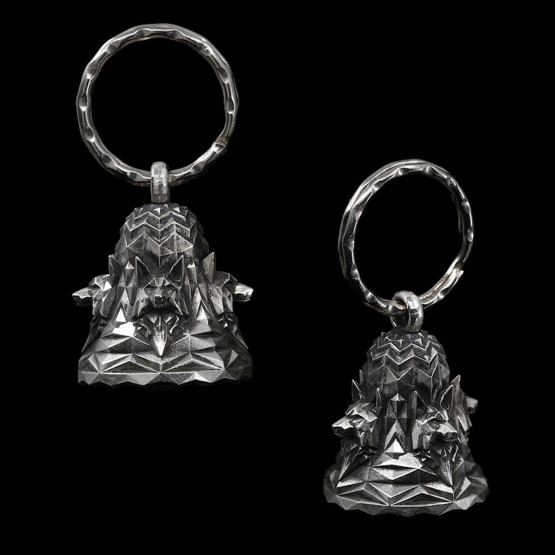 May include: Two silver keychains with geometric bell charms. Each charm features a detailed, faceted design with a textured surface.