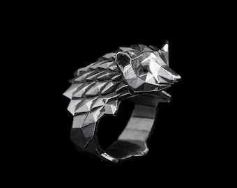 May include: A silver-colored ring featuring a geometric, polygonal design of a bear's head. The bear's head is detailed with triangular facets, and the ring has a smooth band. The ring is set against a black background.