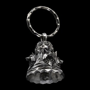May include: A silver bell with a geometric design and a ring at the top. The bell is decorated with small animal figures.