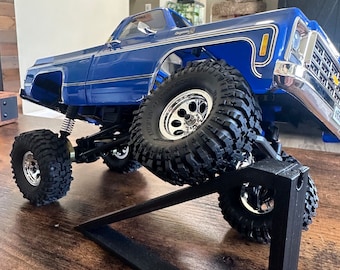 Pode incluir: Um caminhão modelo azul e prata com pneus grandes é exibido em um suporte preto. O caminhão está em uma superfície de madeira.
