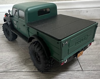 May include: A green toy truck with a black bed cover. The truck has a black license plate that says "BOBBY".