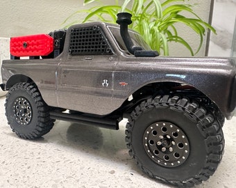 May include: A gray and black toy truck with a red bed and black wheels. The truck has a black mesh window and a black exhaust pipe.