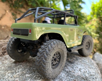 May include: A green toy truck with a black roll cage and black wheels. The truck is on a rocky surface.