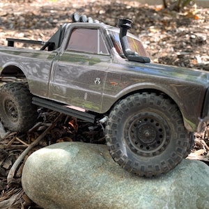 Könnte beinhalten: Ein grauer und schwarzer Spielzeug-LKW mit einem schwarzen Überrollbügel und einem schwarzen Schnorchel. Der LKW steht auf einem Stein mit braunem Mulch im Hintergrund.