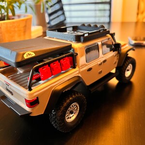 May include: A tan Jeep Wrangler pickup truck with a black roof rack, a black roof top tent, and red gas cans on the back.