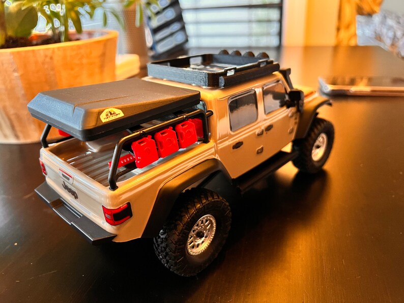 May include: A tan Jeep Wrangler pickup truck with a black roof rack, a black roof top tent, and red gas cans on the back.