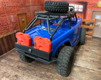 May include: A blue toy truck with a black roll cage and a spare tire on the roof. The truck has two red fuel canisters on the back.