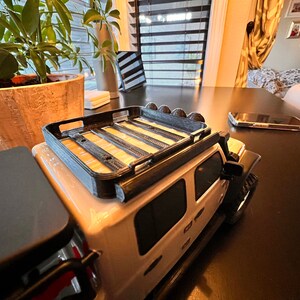 May include: A white toy Jeep with a black roof rack and black wheels. The Jeep is sitting on a dark brown table.