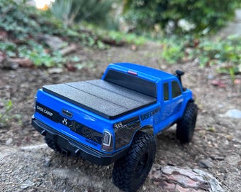 Puede incluir: Un camión de juguete azul con una cubierta de cama negra y "BASE CAMP" escrito en el lateral. El camión tiene ruedas negras y una pegatina 4x4 en el lateral.