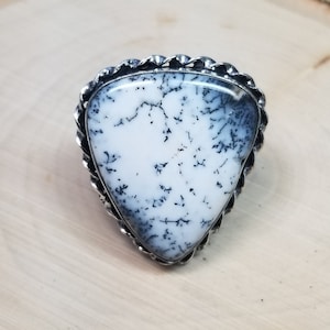 May include: A silver ring with a triangular dendritic agate stone. The stone is white with black dendritic patterns.