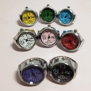 Puede incluir: Ocho relojes de pulsera de plata con diferentes caras de colores. Las caras son amarillas, verdes, azules, blancas, rosas, rojas, moradas y negras.