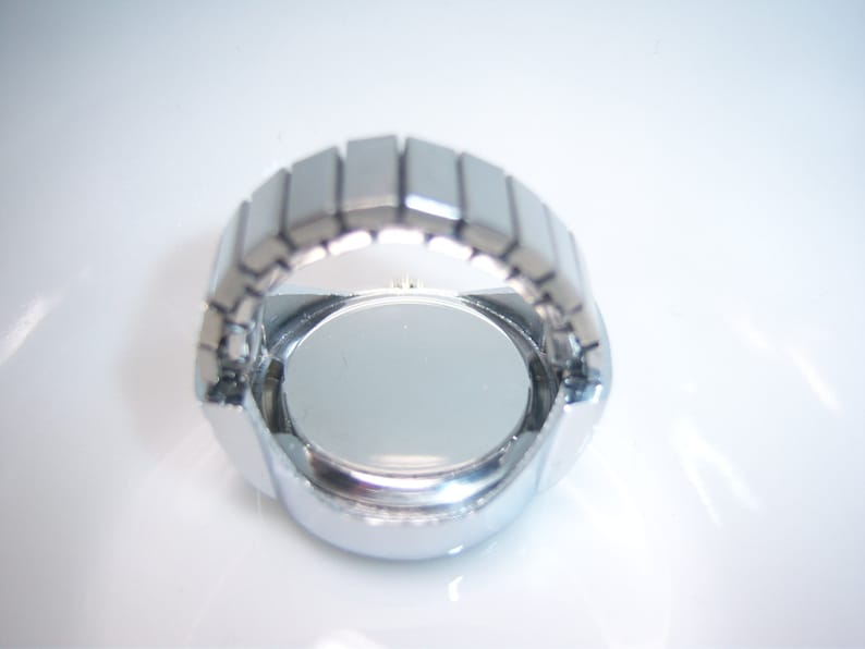 Puede incluir: Reloj de pulsera plateado con esfera redonda y correa de metal. El reloj se muestra desde la parte posterior, revelando la caja de metal.