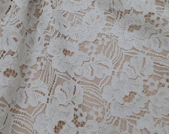 May include: White floral lace fabric with a delicate pattern. The fabric has a soft, flowing texture and is perfect for creating garments, accessories, or home decor.