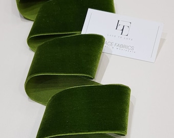 May include: A close-up of a spool of dark green velvet ribbon. The ribbon is folded in a spiral shape, showing the soft texture of the fabric. The ribbon is labeled "Lace to Love Lace Fabrics"
