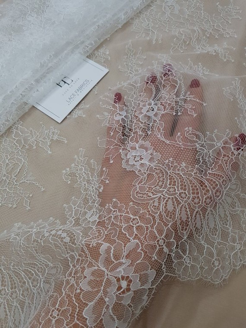 May include: White floral lace fabric with a delicate pattern. The lace is sheer and has a soft, flowing texture.