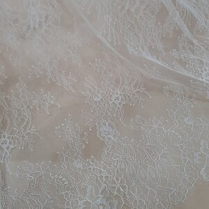 May include: White lace fabric with a delicate floral pattern. The lace is sheer and has a soft, flowing texture.