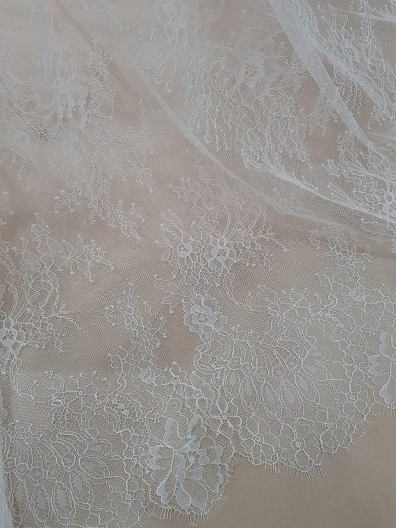 May include: White lace fabric with a delicate floral pattern. The lace is sheer and has a soft, flowing texture.