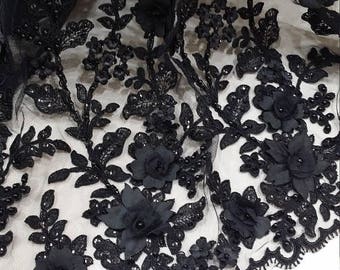 May include: A black lace fabric featuring three-dimensional floral appliqués, intricate embroidery, and scattered sequins. The sheer mesh base is adorned with detailed leaf patterns and small beads, finished with a scalloped edge along the bottom.