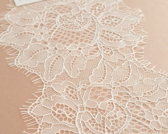 Könnte beinhalten: Weiße Spitzenborte mit zartem Blumenmuster. Die Spitze hat einen gewellten Rand und ist perfekt, um jedem Projekt einen Hauch von Eleganz zu verleihen.