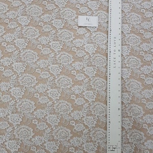 May include: White floral lace fabric featuring a repeating pattern of embroidered flowers and sequins. A ruler with centimetre measurements is visible, along with a tag that reads "Lace Fabrics". The text "Lace to Love" is printed on the ruler.