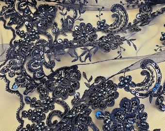 May include: Navy blue lace fabric featuring intricate floral embroidery, embellished with matching dark blue beads, small pearls, and shimmering sequins. The delicate mesh netting provides a sheer base for the detailed needlework.