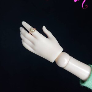May include: A gold heart-shaped ring with a smooth, polished finish. The ring is worn on the index finger of a hand.