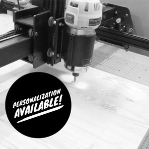 Puede incluir: Una imagen en blanco y negro de una fresadora CNC grabando una pieza de madera. La fresadora est&aacute; cortando las palabras "on a life" en la madera. Un c&iacute;rculo negro con texto blanco que dice "&iexcl;Personalizaci&oacute;n disponible!" est&aacute; en primer plano.