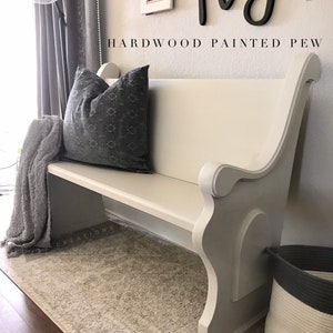 May include: A white painted wooden bench with a gray blanket and pillow. The bench has a curved back and arms. The bench is in front of a wall with the word "play" written in black letters. The text "HARDWOOD PAINTED PEW" is written below the word "play".